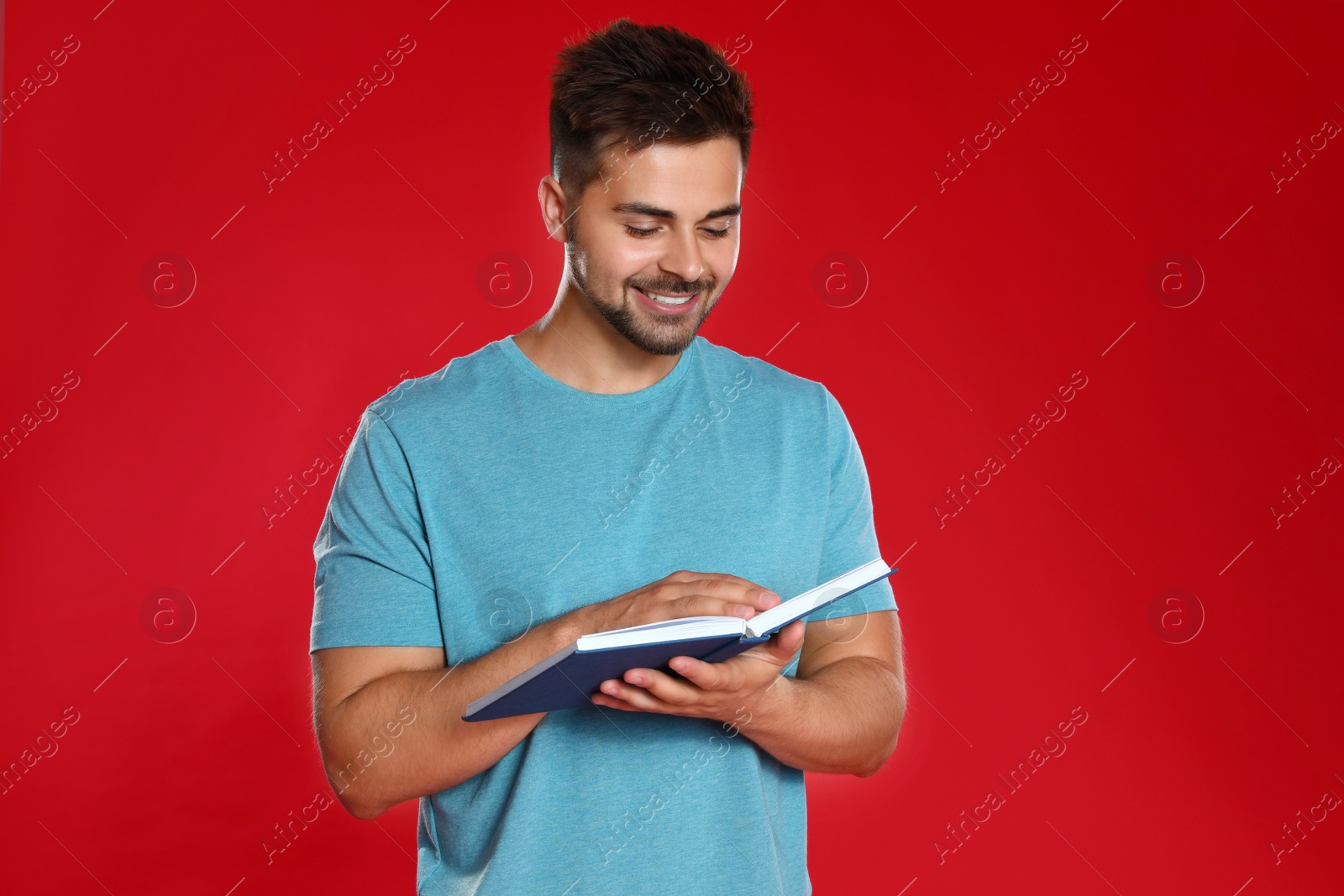 Photo of Handsome young man reading book on red background