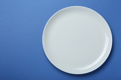 Empty white ceramic plate on blue background, top view. Space for text