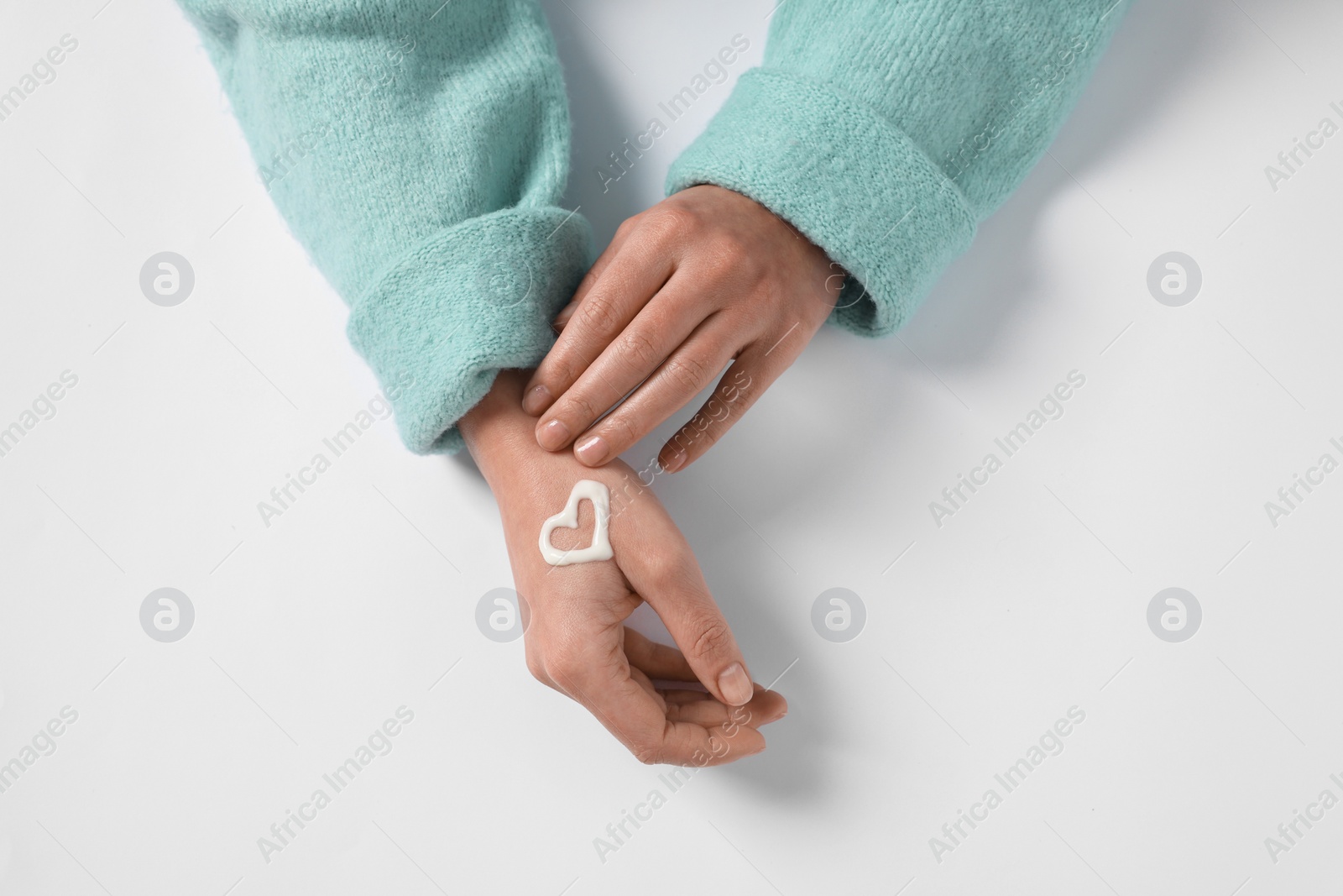 Photo of Woman with heart made of cosmetic cream on hand against white background, top view