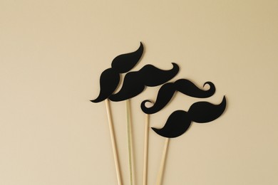 Fake paper mustaches party props on beige background, flat lay. Space for text