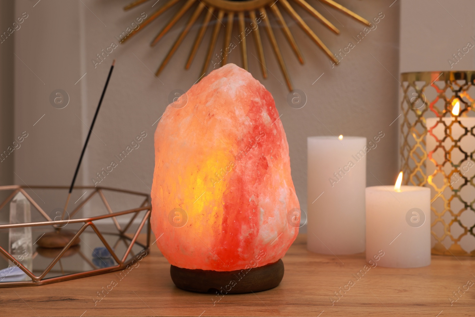 Photo of Himalayan salt lamp, candles and crystals on wooden table near white wall indoors