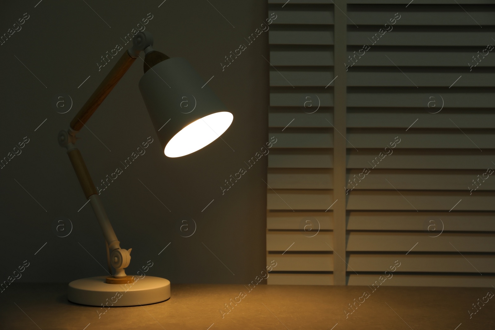 Photo of Stylish modern desk lamp on table at night, space for text