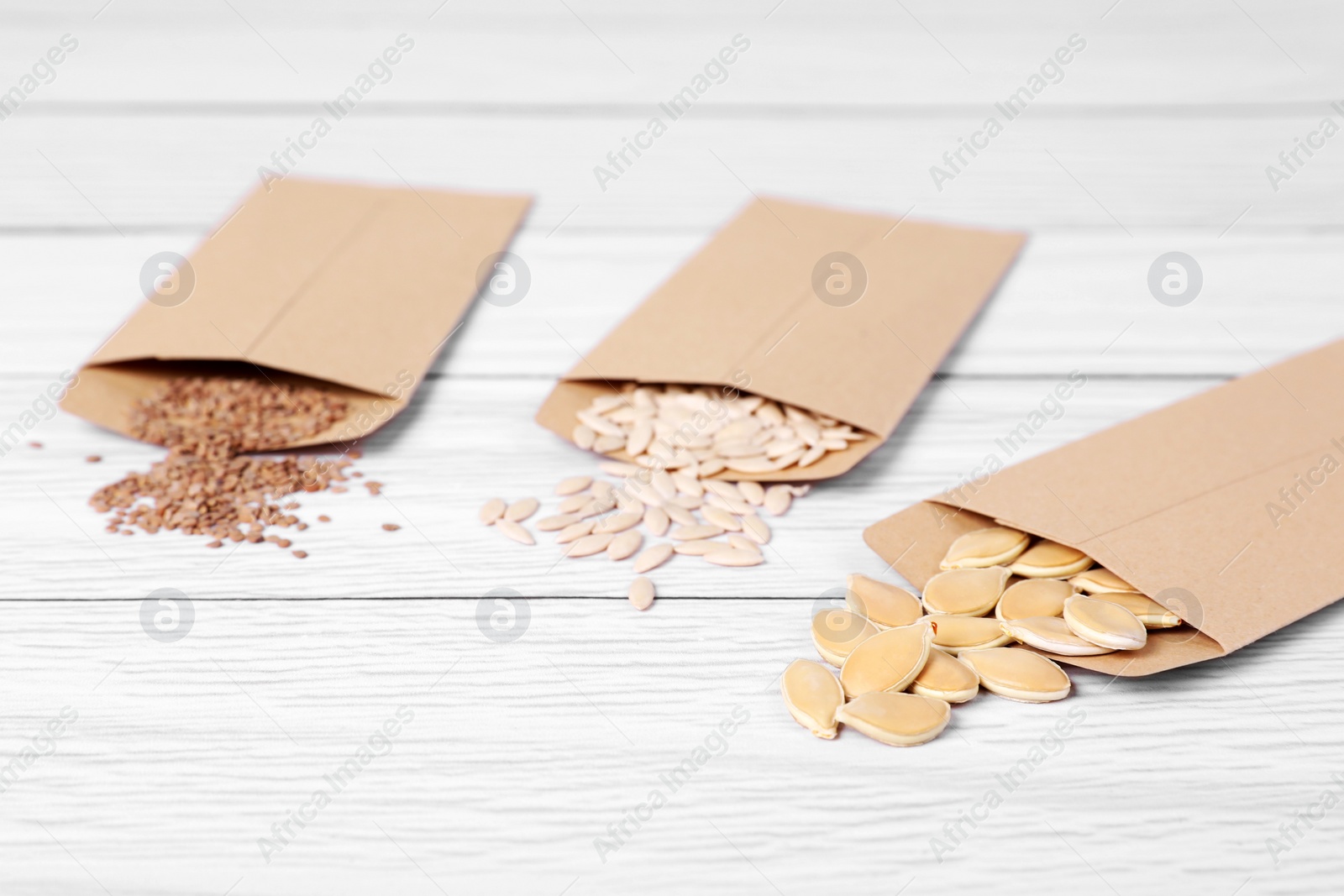 Photo of Many different vegetable seeds on white wooden table, closeup