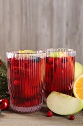 Photo of Aromatic Sangria drink in glasses, ingredients and Christmas decor on wooden table