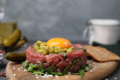 Photo of Tasty beef steak tartare served with yolk, pickled cucumber and other accompaniments on table, closeup