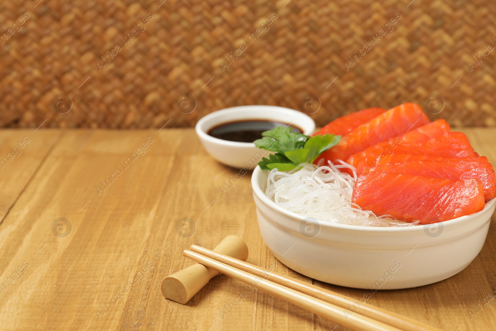 Photo of Delicious salmon sashimi served with funchosa, soy sauce and parsley on wooden table, closeup. Space for text