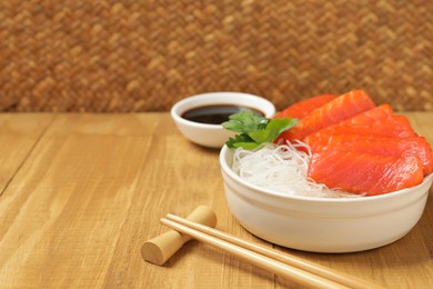 Photo of Delicious salmon sashimi served with funchosa, soy sauce and parsley on wooden table, closeup. Space for text