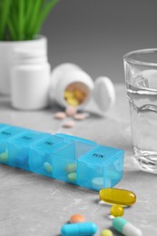 Weekly pill box with medicaments and glass of water on grey marble table, closeup