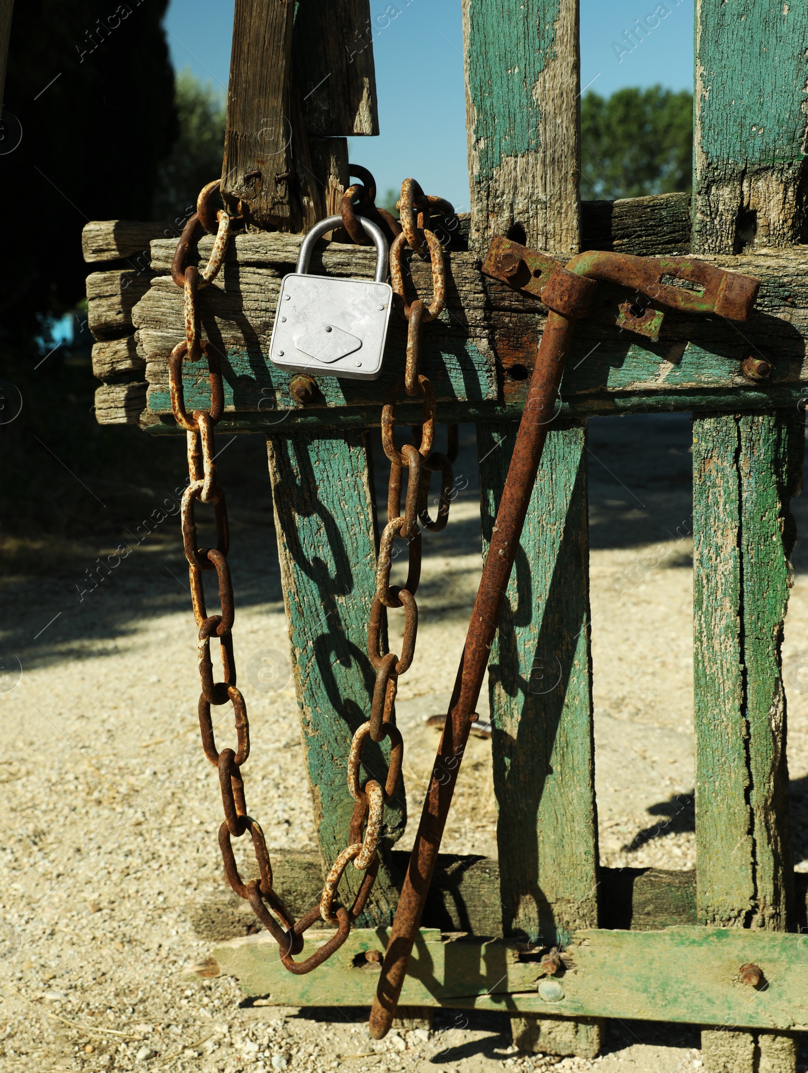 Photo of Old wooden fence with metal chain and lock on sunny day