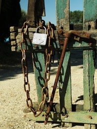 Photo of Old wooden fence with metal chain and lock on sunny day