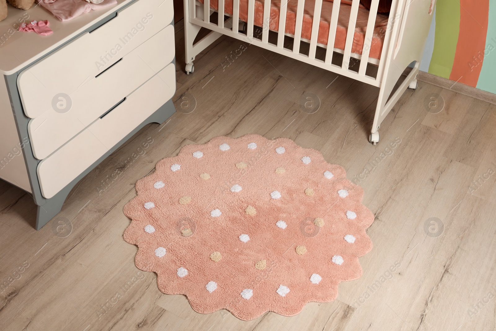 Photo of Round pink rug with polka dot pattern on wooden floor in baby's room, above view