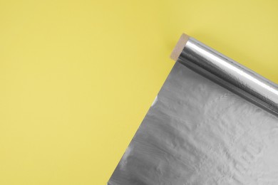 Photo of Roll of aluminum foil on yellow background, top view. Space for text