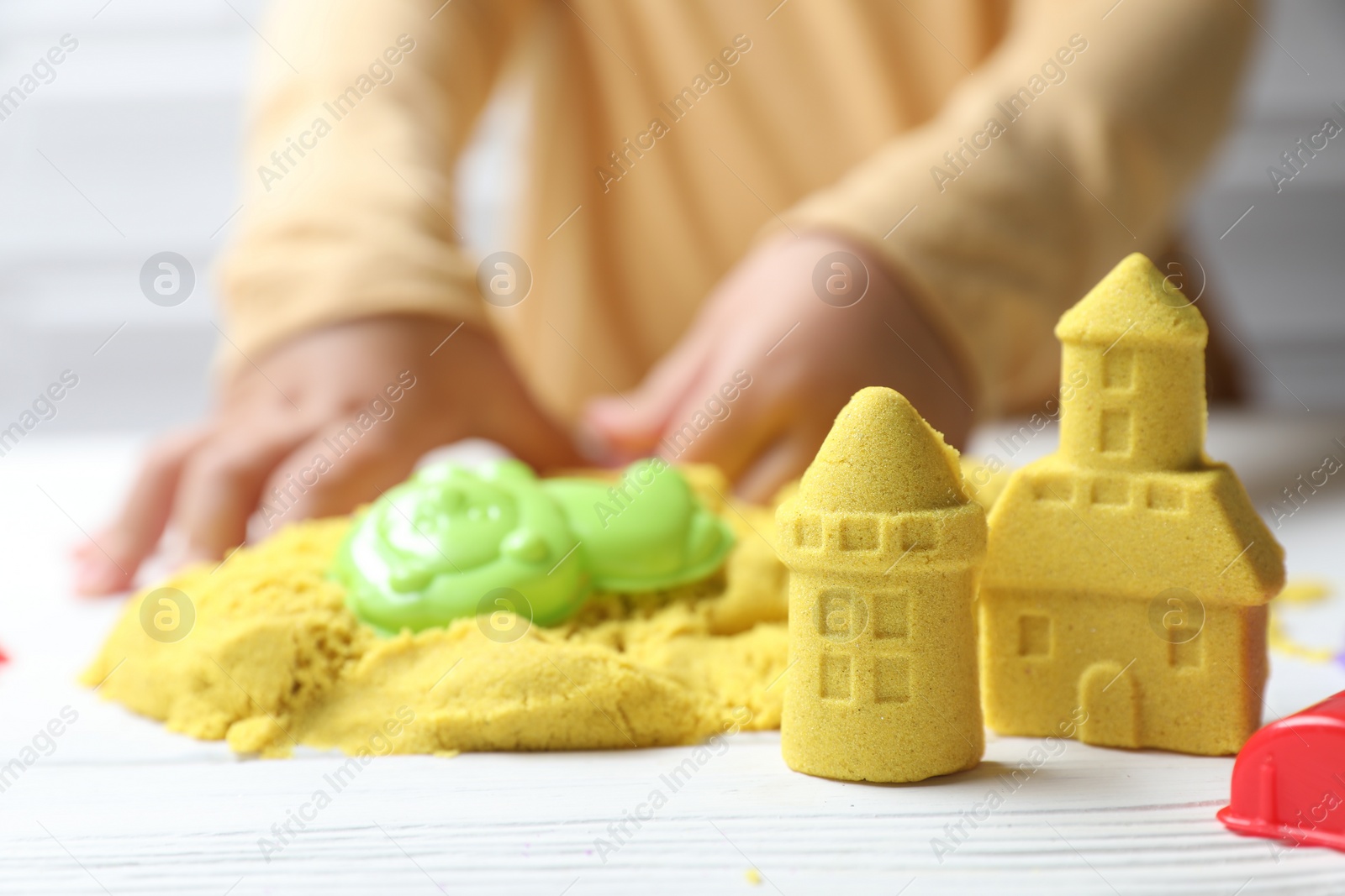 Photo of Little child playing with yellow kinetic sand at white wooden table, selective focus