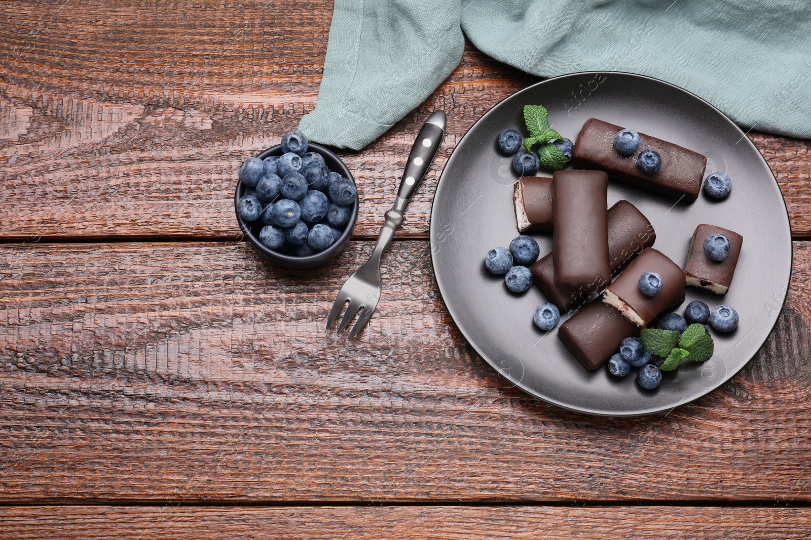 Photo of Delicious glazed curd snacks with blueberries on wooden table, flat lay. Space for text