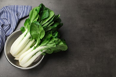 Photo of Fresh green pak choy cabbages with water drops in sieve on grey table, top view. Space for text