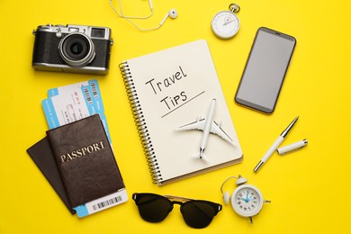 Flat lay composition with phrase Travel Tips written in notebook, passports, tickets and toy airplane on yellow background