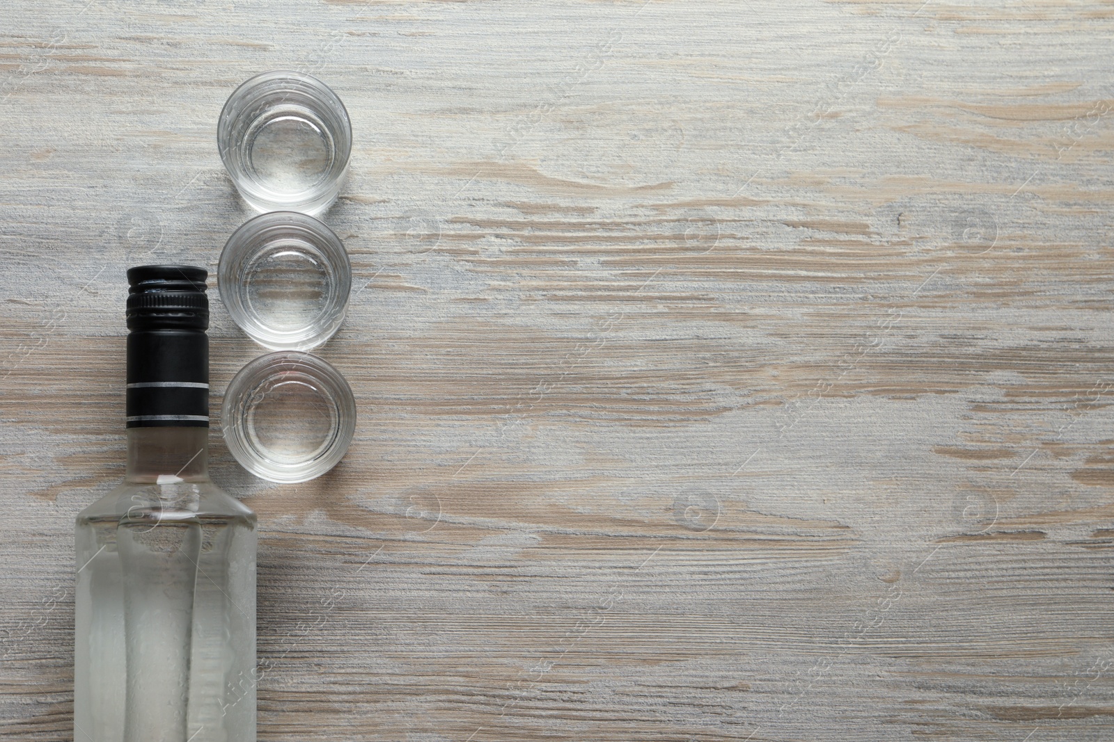 Photo of Bottle and shot glasses of vodka on wooden table, flat lay. Space for text