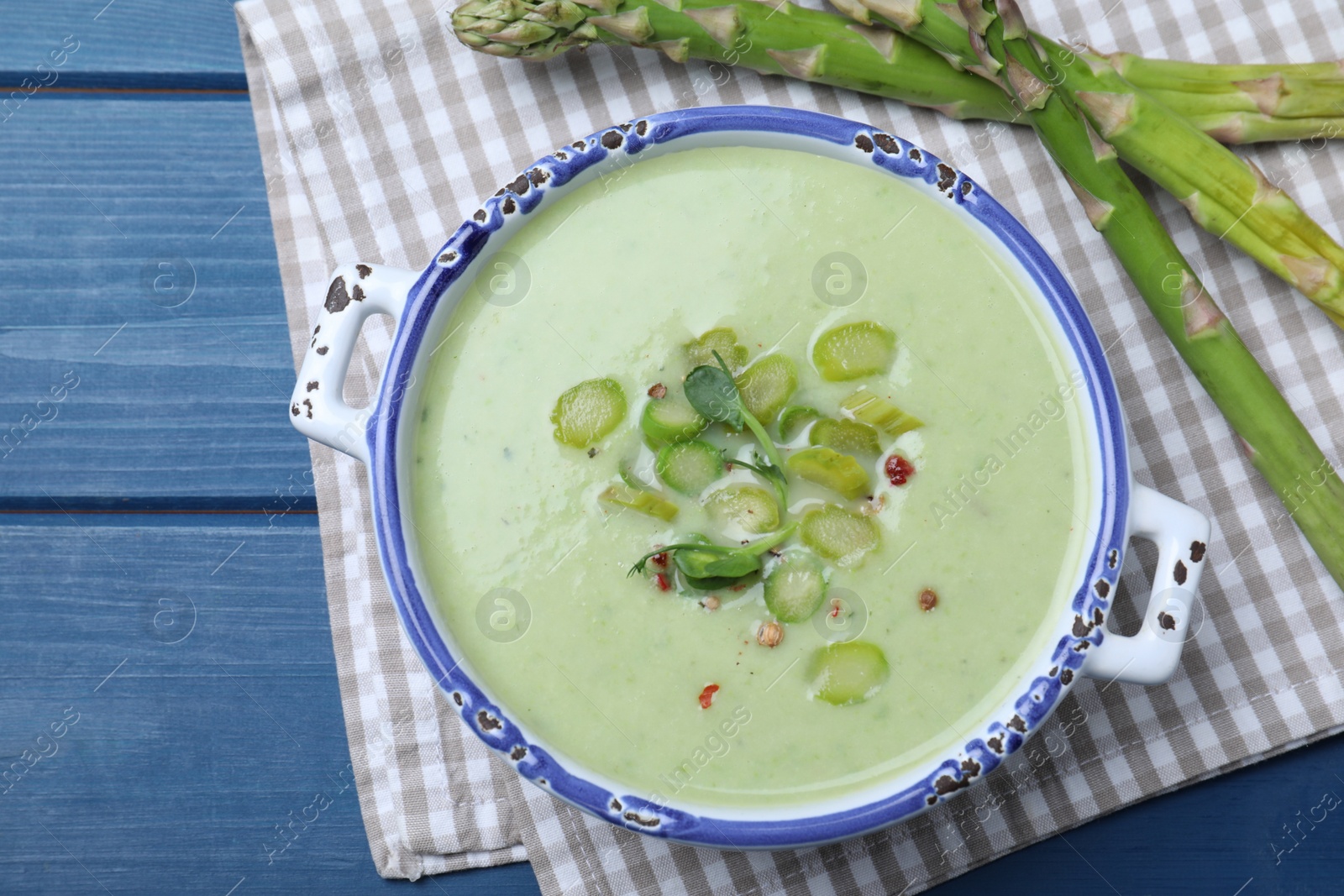 Photo of Delicious asparagus soup served on blue wooden table, flat lay