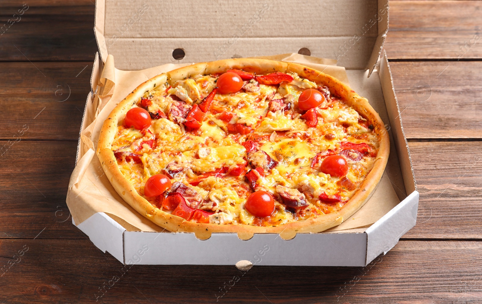 Photo of Cardboard box with delicious pizza on wooden table
