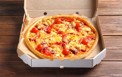 Photo of Cardboard box with delicious pizza on wooden table