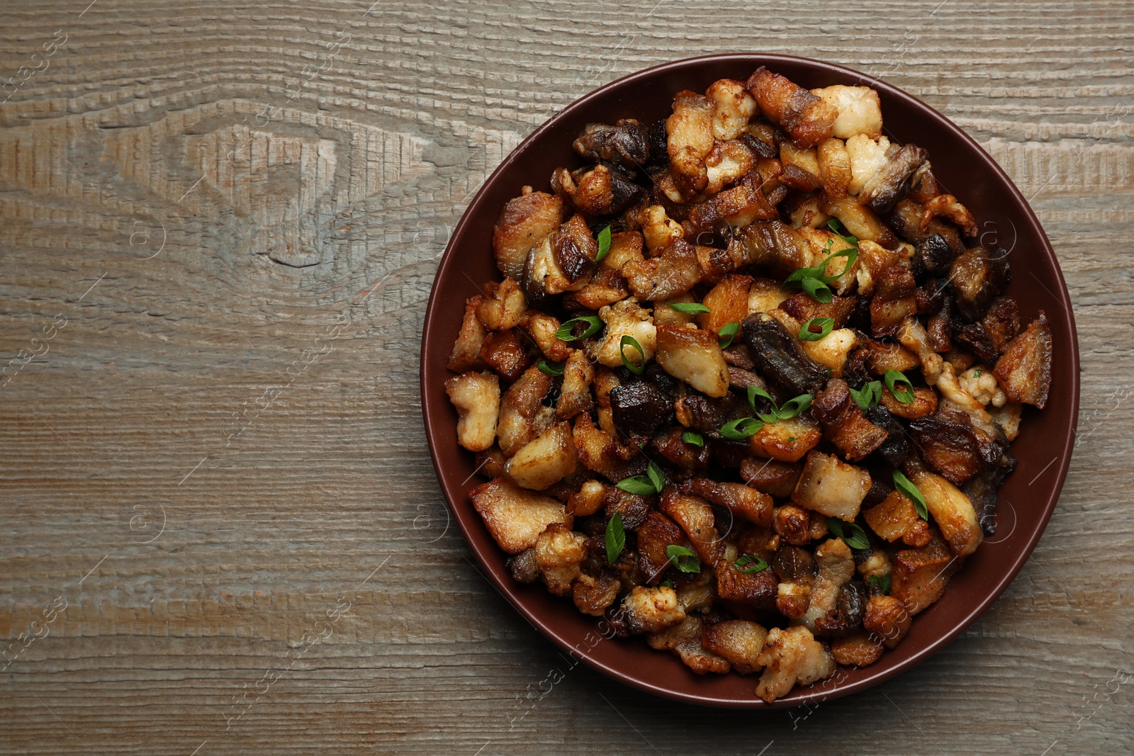 Photo of Tasty fried cracklings on wooden table, top view with space for text. Cooked pork lard