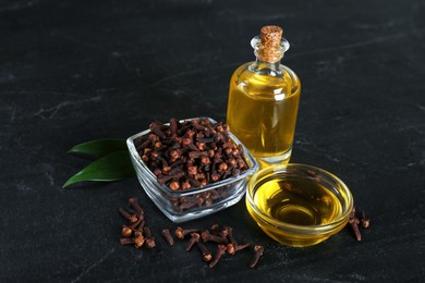 Photo of Essential oil and dried cloves on black table