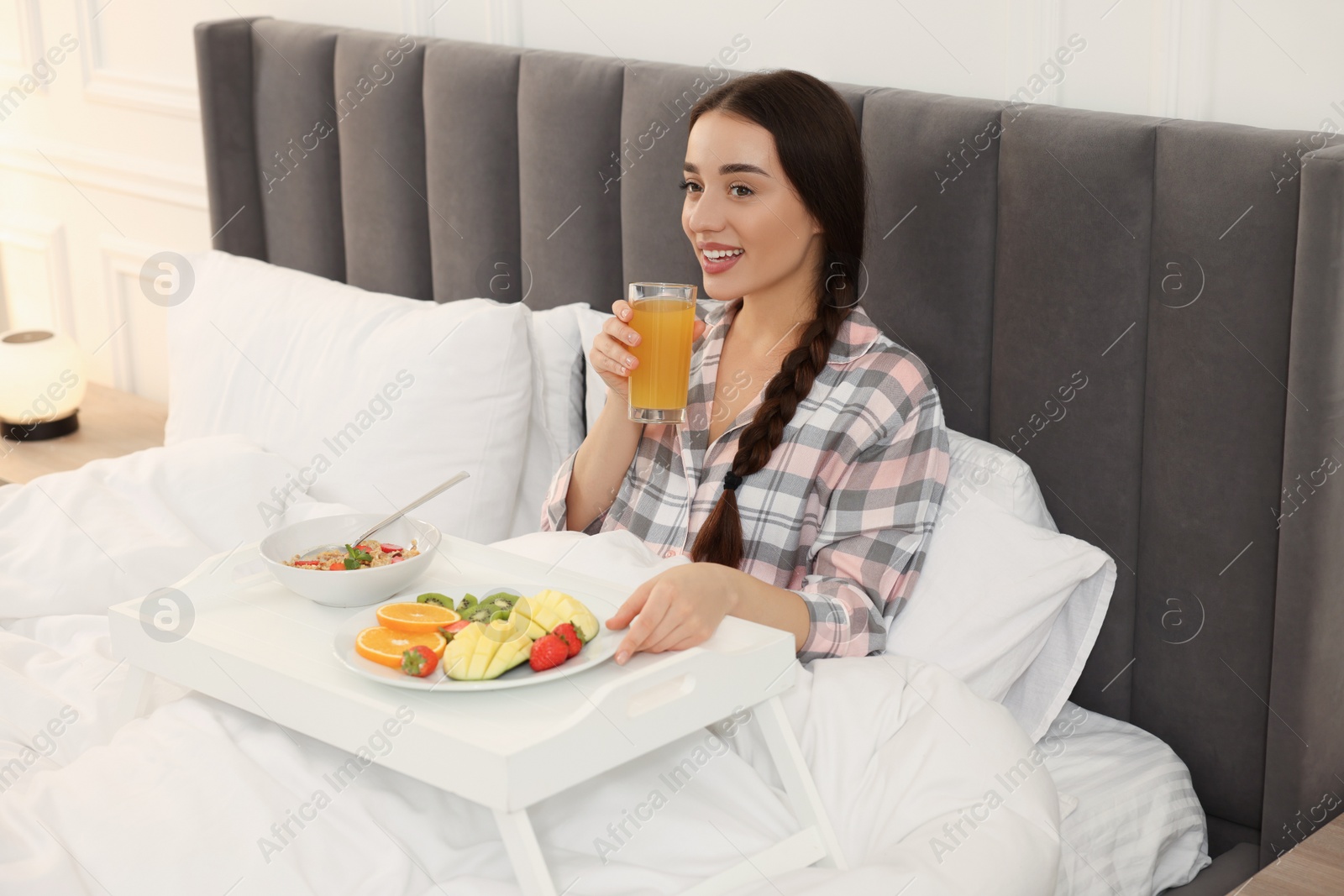 Photo of Happy young woman having breakfast on bed at home