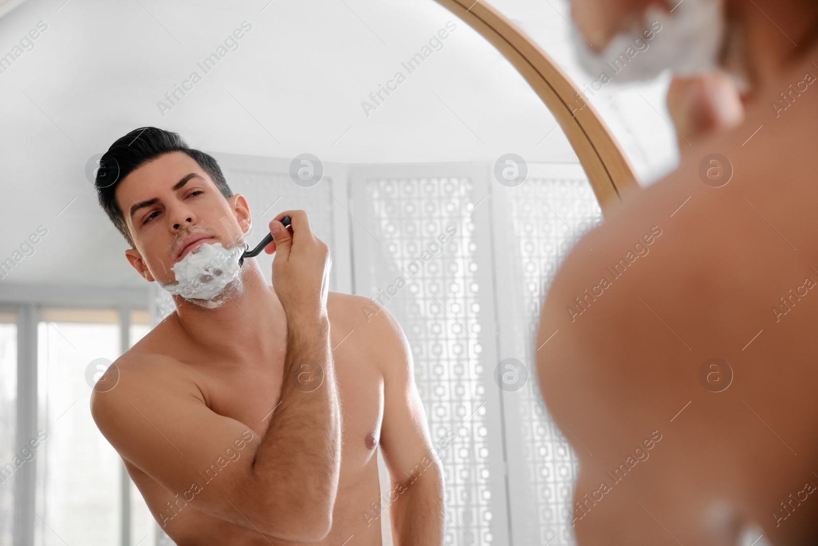 Photo of Handsome man shaving near mirror in bathroom