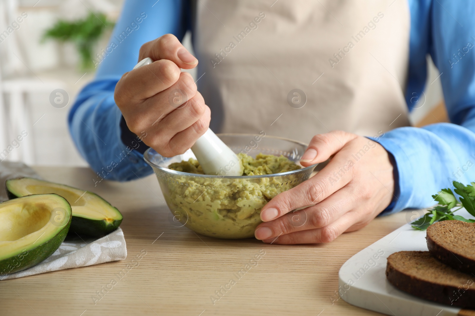 Photo of Woman preparing guacamole of ripe avocados at wooden table indoors, closeup