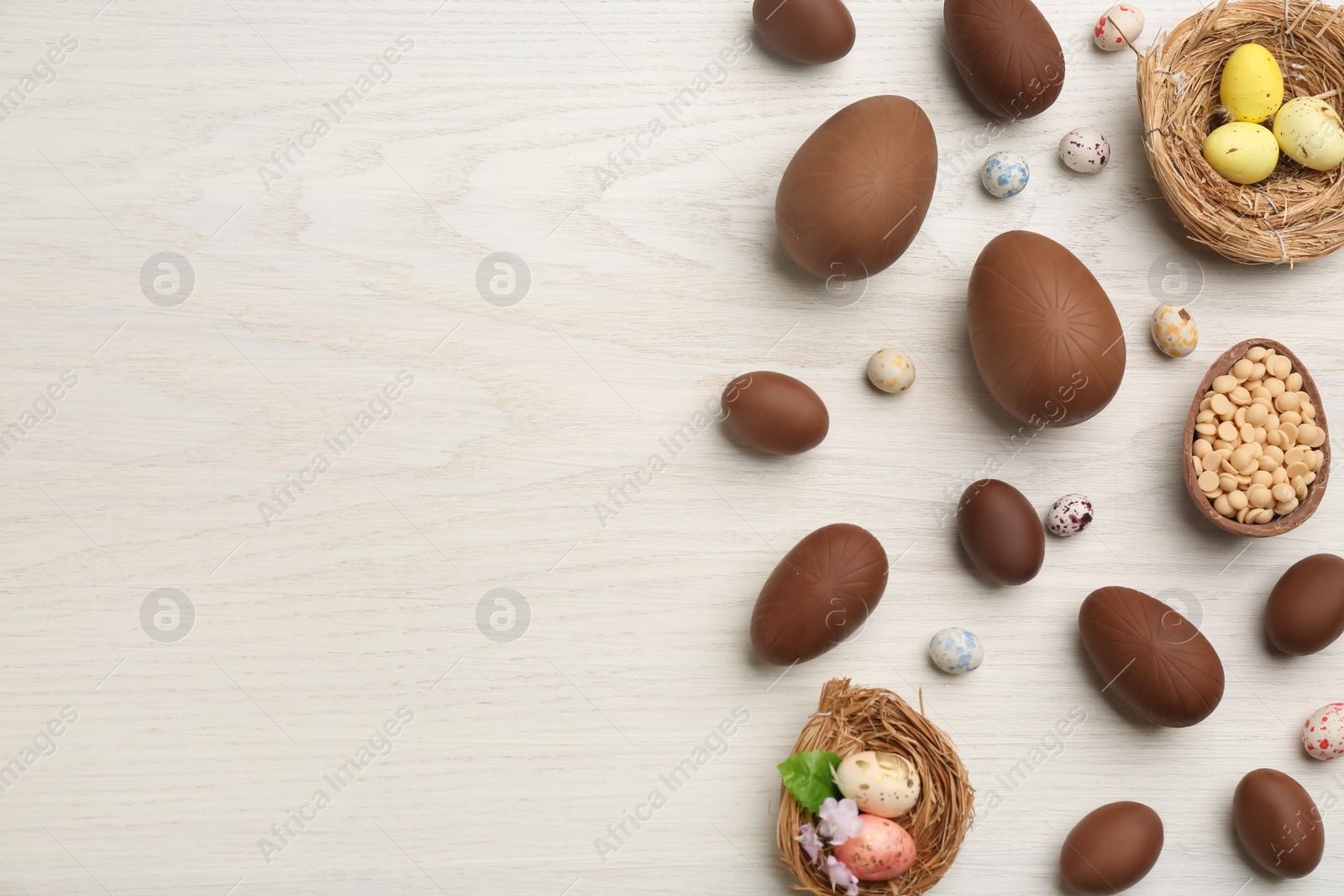 Photo of Sweet chocolate eggs and candies on white wooden table, flat lay. Space for text