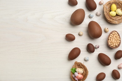 Photo of Sweet chocolate eggs and candies on white wooden table, flat lay. Space for text