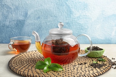 Photo of Teapot with hot aromatic tea, dry and fresh leaves on wicker mat