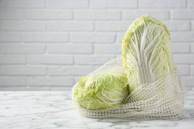 Photo of Fresh Chinese cabbages in string bag on white marble table near brick wall. Space for text