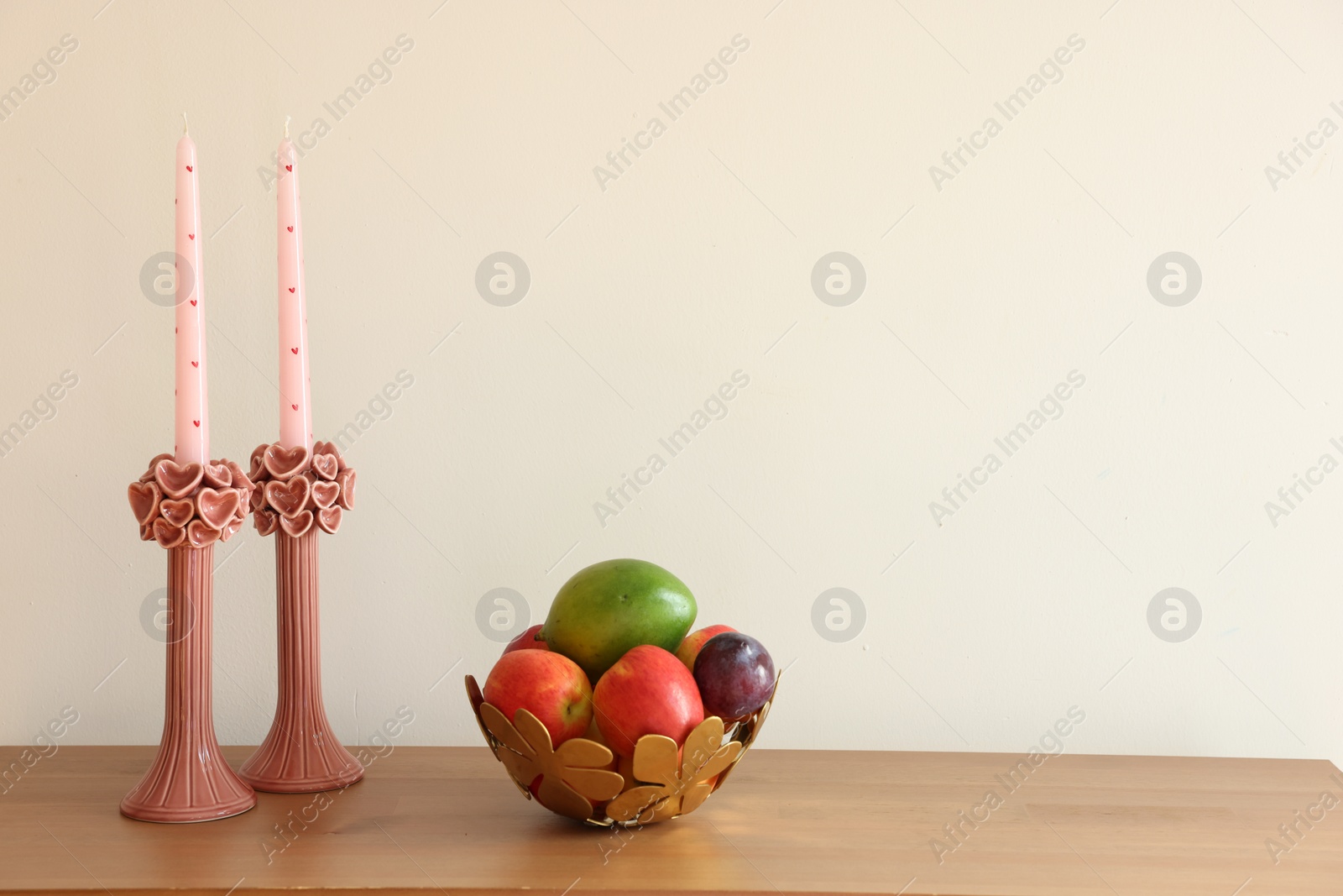 Photo of Beautiful pink wax candles and bowl with fresh fruits on wooden table near white wall. Space for text