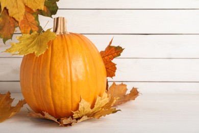 Photo of Fresh ripe pumpkin and dry leaves on white table, space for text