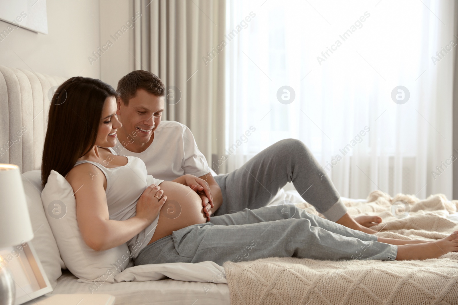 Photo of Young pregnant woman with her husband in bedroom