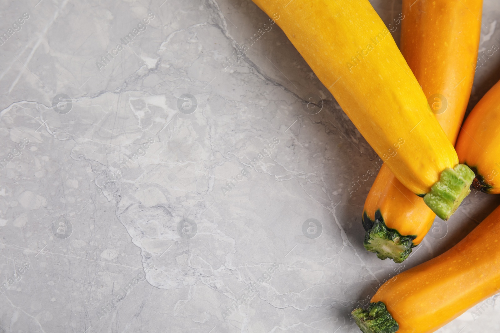 Photo of Fresh ripe yellow zucchini on grey marble background, flat lay. Space for text