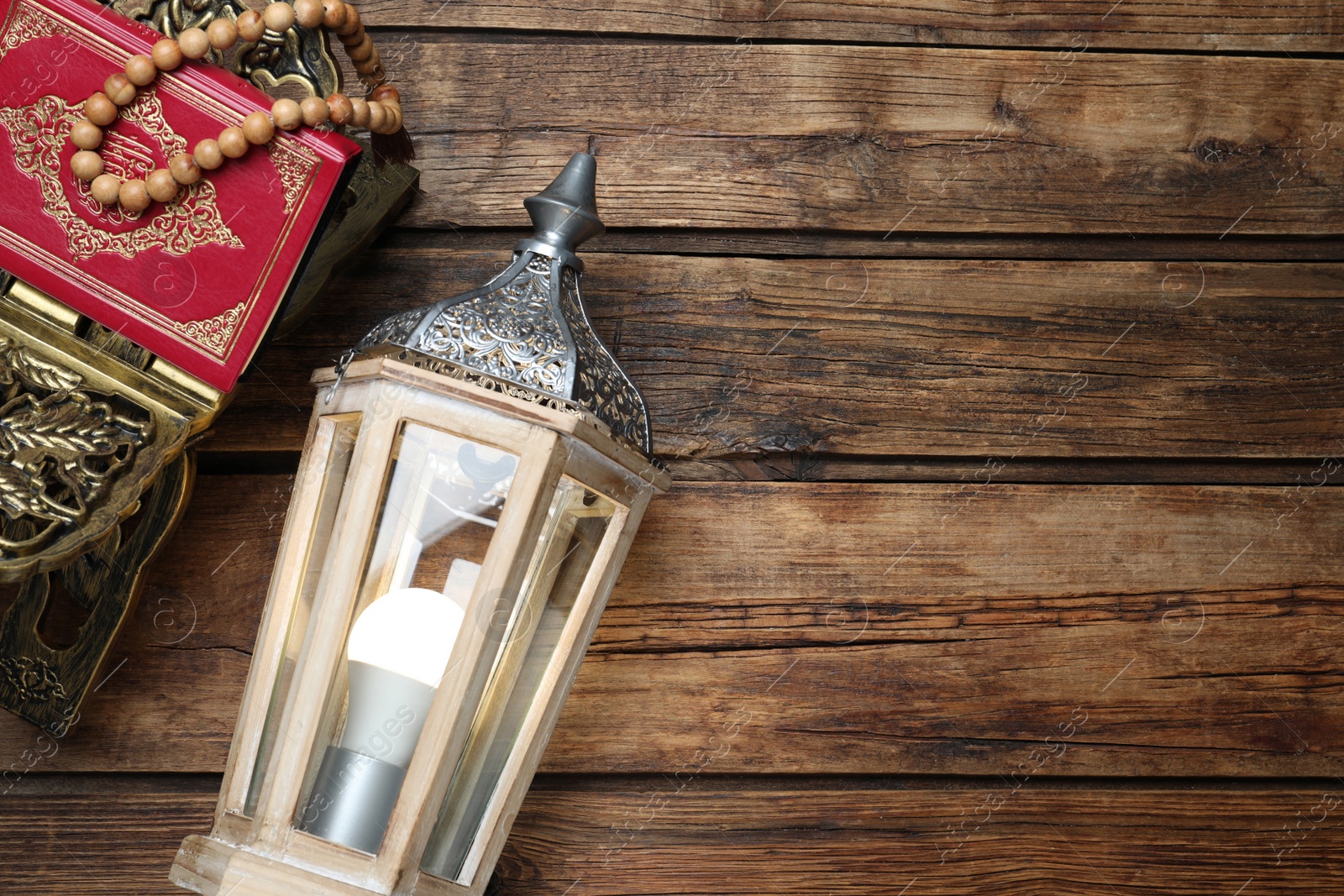 Photo of Arabic lantern, quran and misbaha on wooden table, flat lay. Space for text