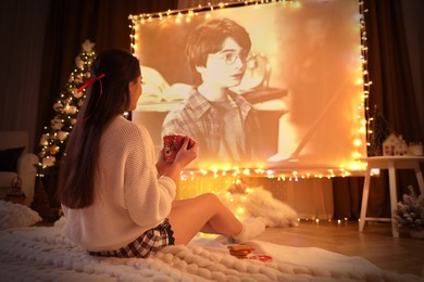 MYKOLAIV, UKRAINE - DECEMBER 24, 2020: Woman watching Harry Potter and Philosopher's Stone movie via video projector in room. Cozy winter holidays atmosphere