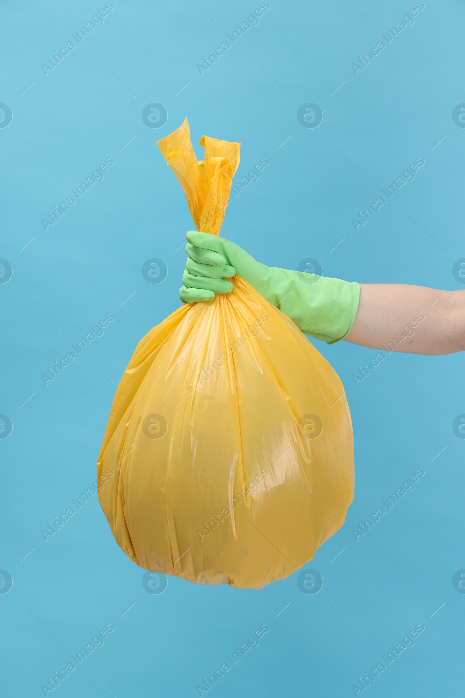 Photo of Woman holding plastic bag full of garbage on light blue background, closeup