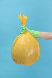 Photo of Woman holding plastic bag full of garbage on light blue background, closeup