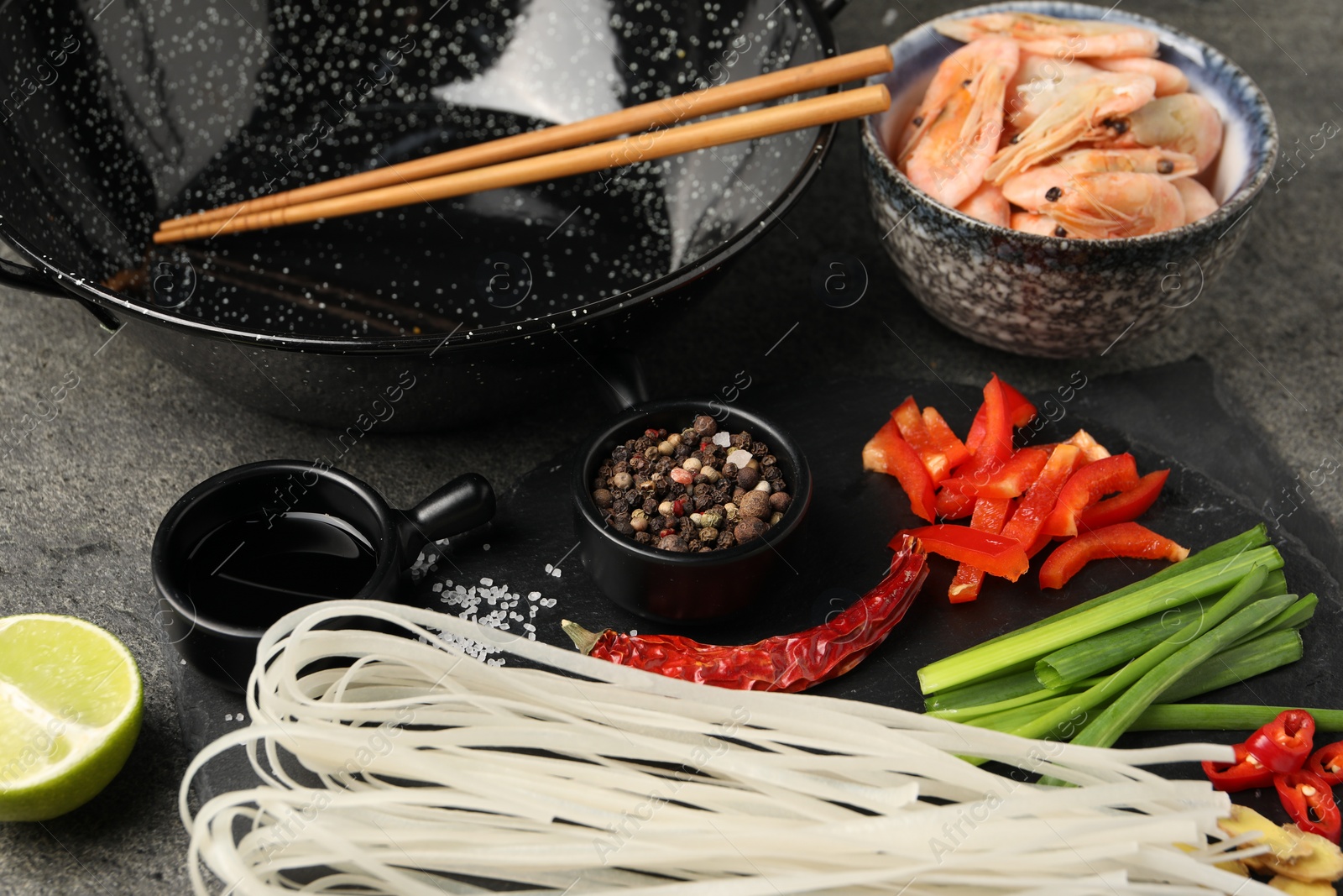 Photo of Different products and wok with chopsticks on dark table, closeup