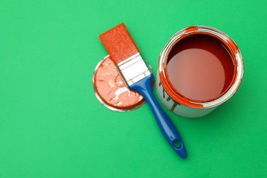 Photo of Can of orange paint and brush on green background, flat lay. Space for text