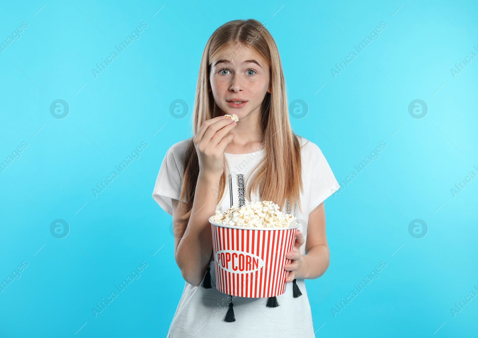 Photo of Emotional teenage girl with popcorn during cinema show on color background