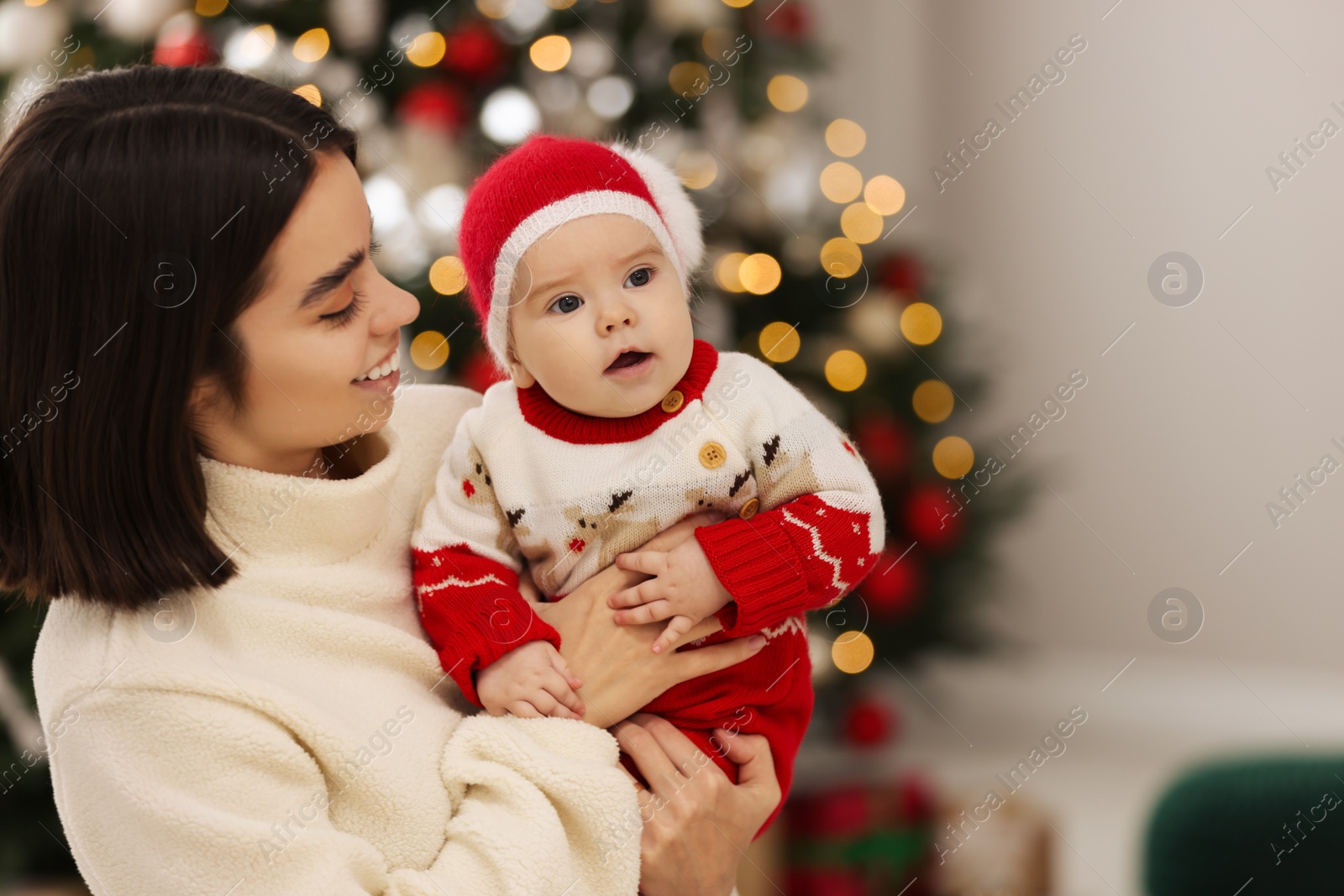 Photo of Happy young mother with her cute baby against blurred festive lights, space for text. Winter holiday