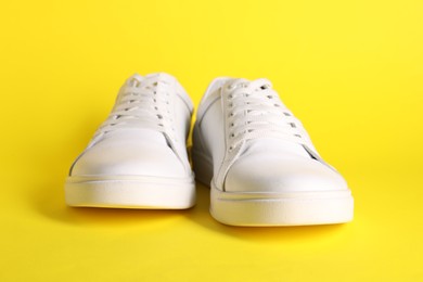 Pair of stylish white sneakers on yellow background