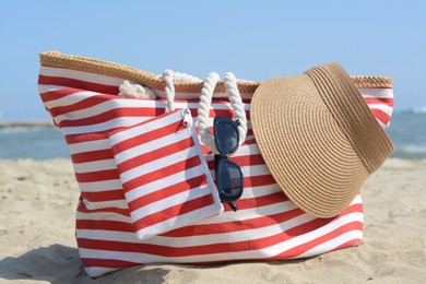 Photo of Stylish striped bag with visor cap and sunglasses on sandy beach near sea
