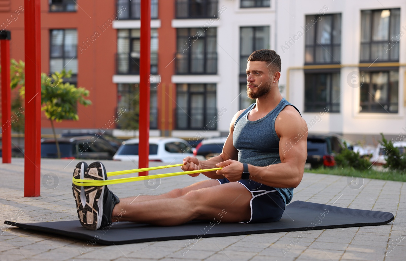 Photo of Muscular man doing exercise with elastic resistance band on mat at sports ground