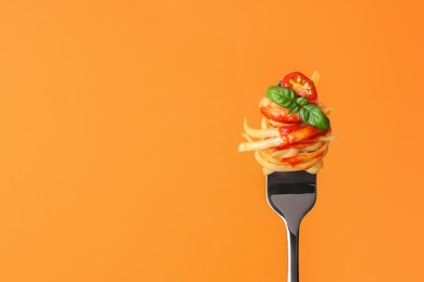 Photo of Tasty pasta with tomato sauce and basil on fork against orange background, space for text