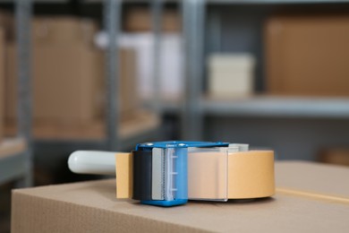 Photo of Adhesive tape dispenser on cardboard box indoors